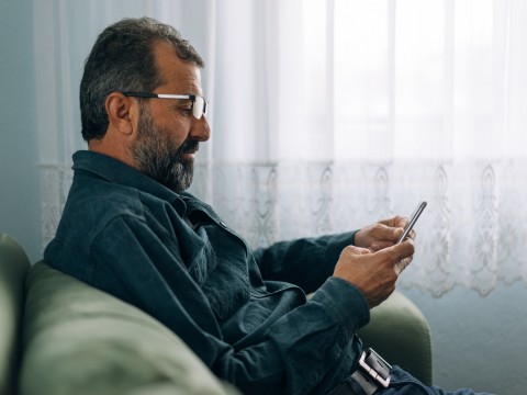 Man sits on couch, looking at smart phone 