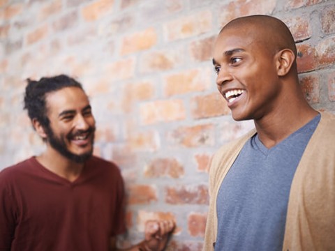 Two men standing and laughing by a brick wall