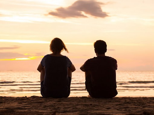 Two people sitting and watching the sunset on a beach
